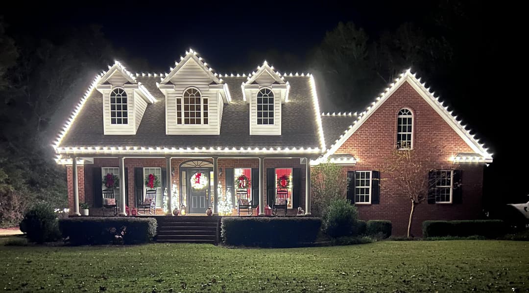Elegant brick house adorned with festive holiday lights and decorations at night.